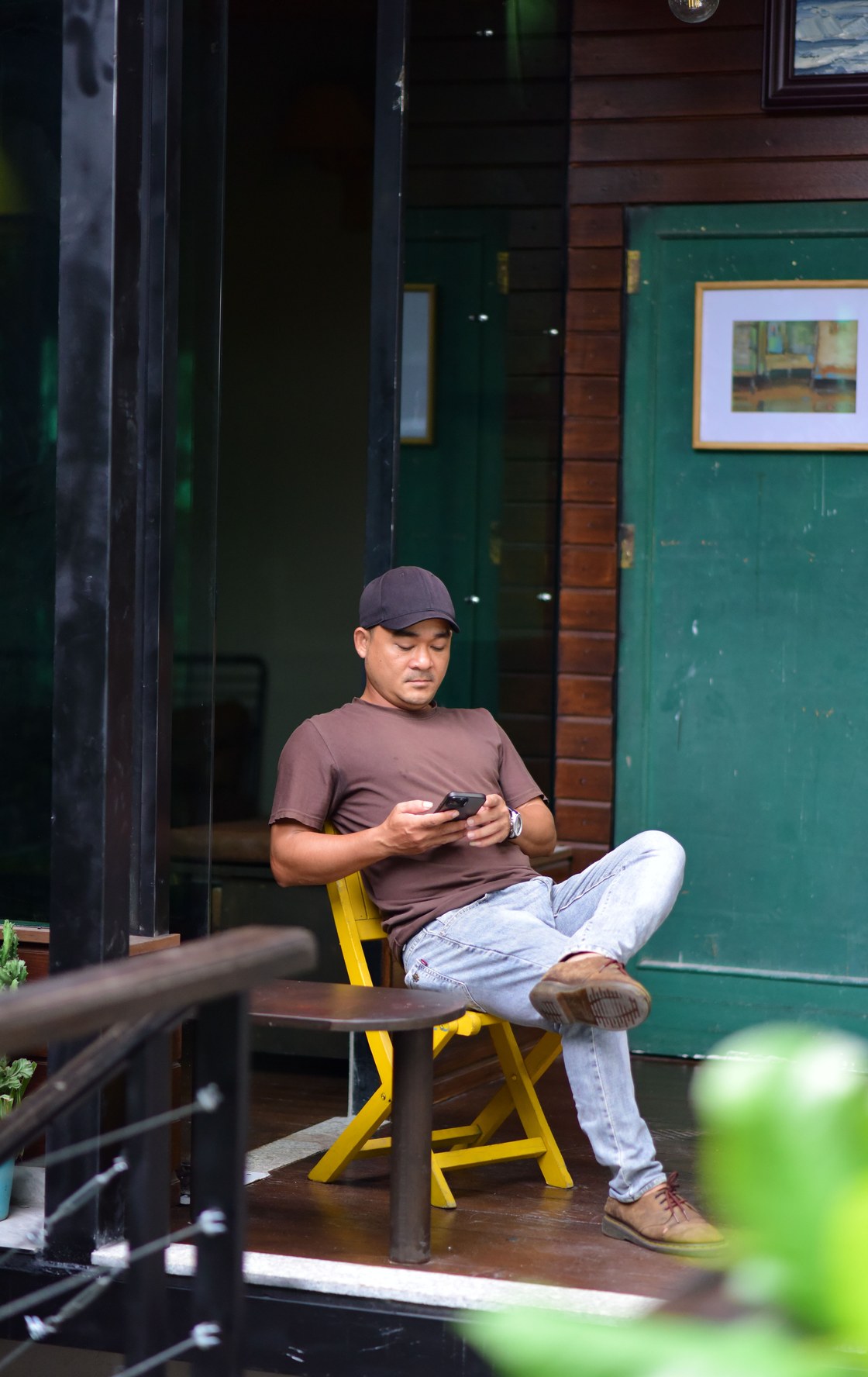Duenno de restaurante sentado fuera, con las piernas cruzadas, mirando el movil