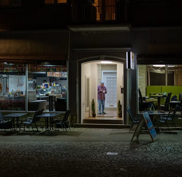 Fachada de un restaurante iluminada de noche, con la puerta abierta