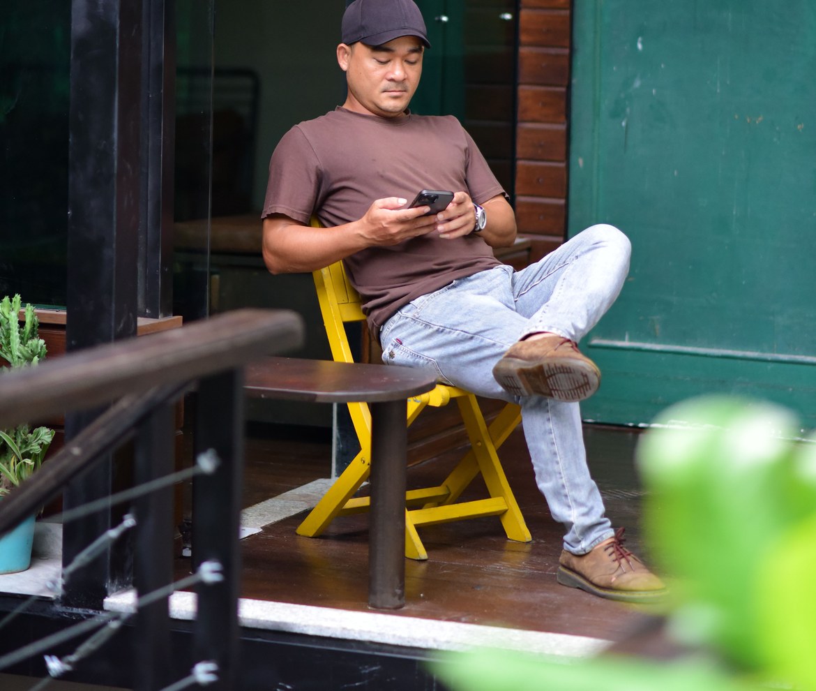 Duenno de restaurante sentado fuera, con las piernas cruzadas, mirando el movil